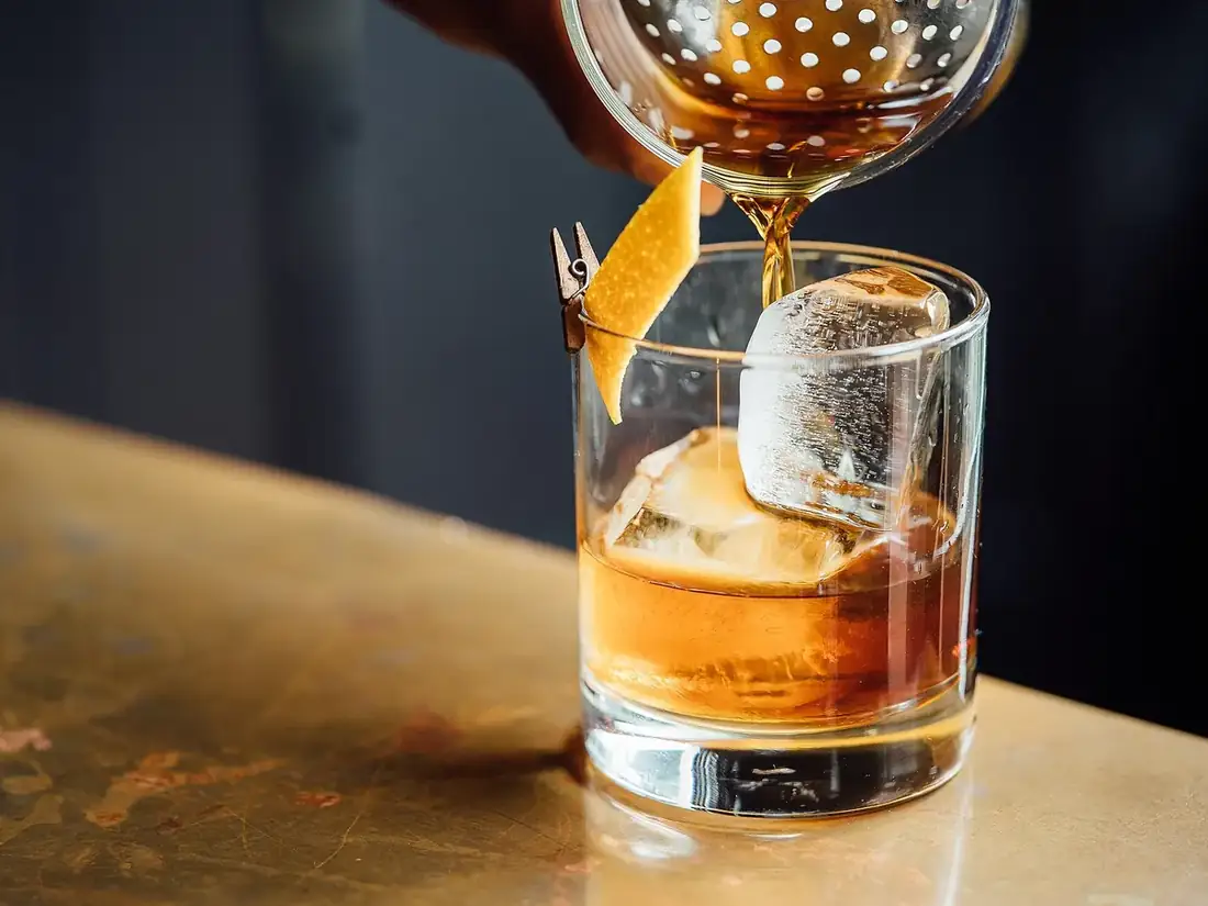 Boisson ambrée versée sur un gros glaçon dans un verre posé sur un comptoir de bar