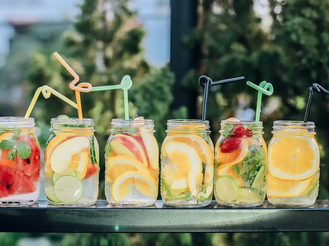 Six bocaux de boissons aux fruits frais avec pailles colorées, alignés sur un rebord de terrasse