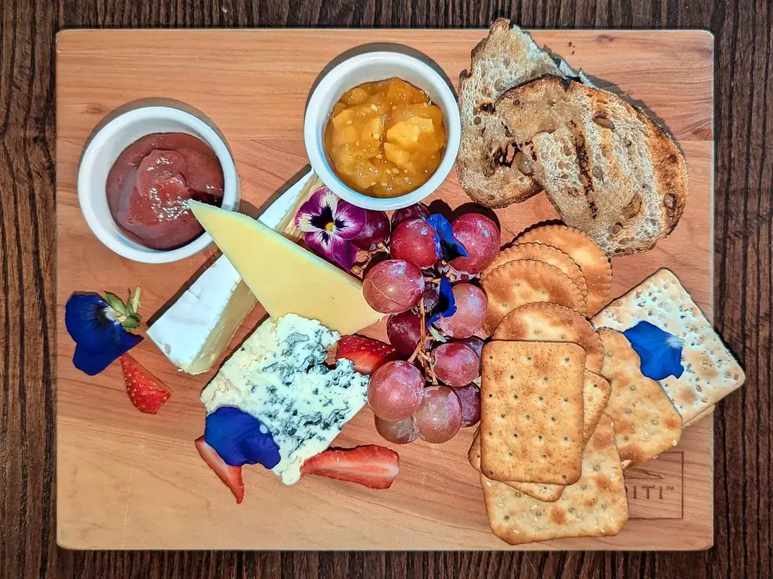 Planche de fromages avec raisin, fraises, crackers, pain grillé et deux petits pots de condiments