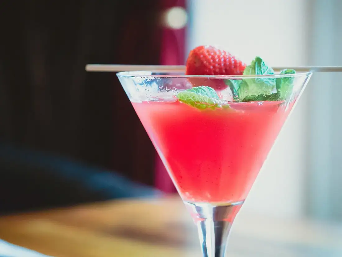 Cocktail rose dans une coupe, garni d'une fraise et de menthe