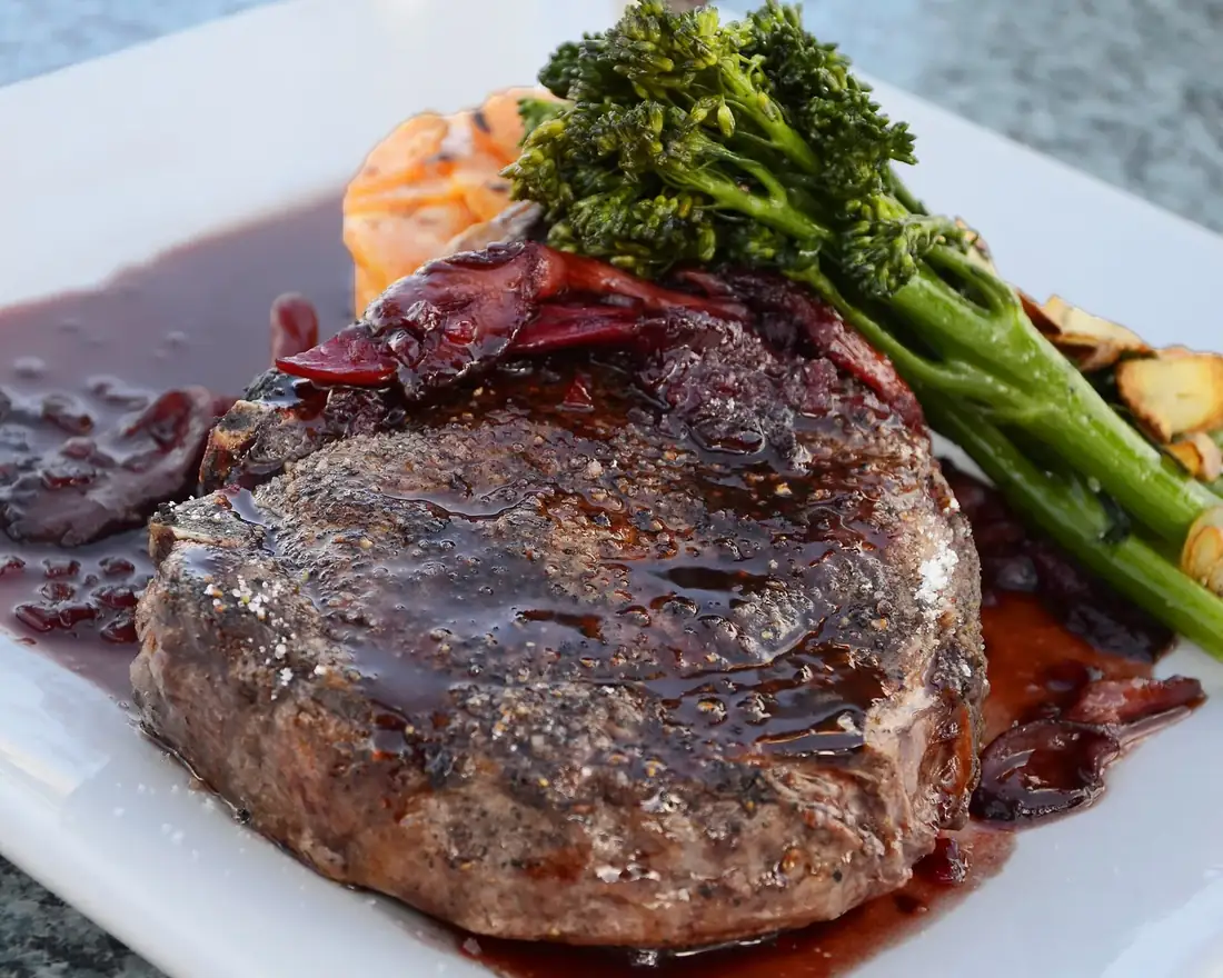 Pavé de bœuf nappé de sauce, servi avec du brocoli sur une assiette blanche carrée
