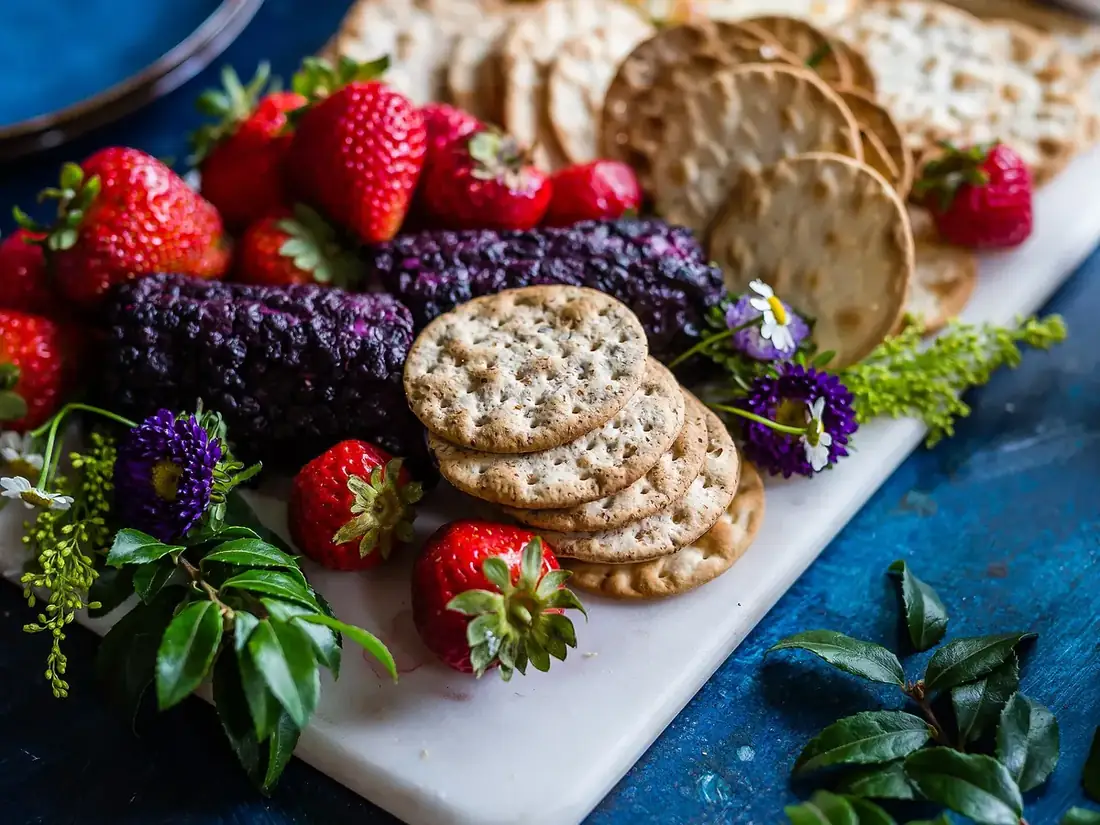 Plateau blanc garni de fraises, de biscuits salés et de fleurs comestibles sur un fond bleu