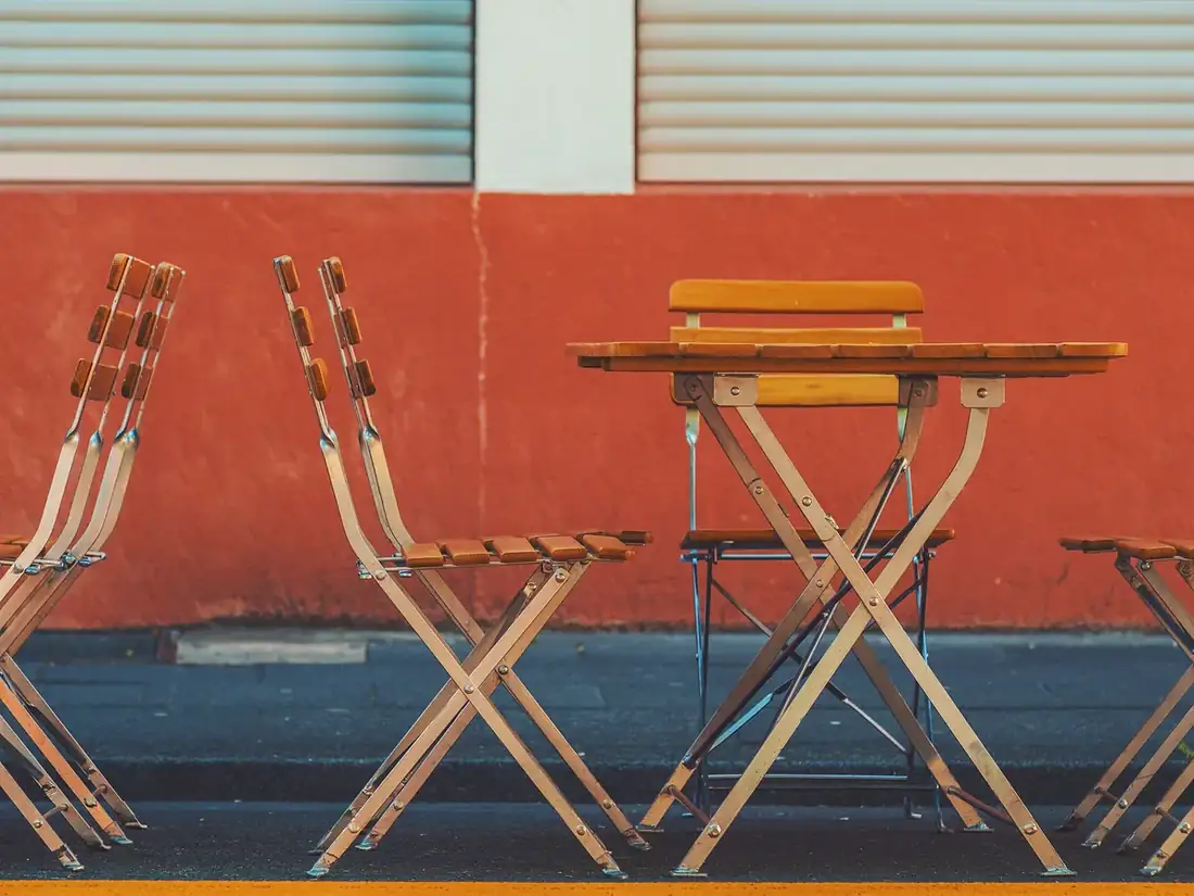 Terrasse de restaurant avec tables et chaises pliantes en bois devant un mur orangé