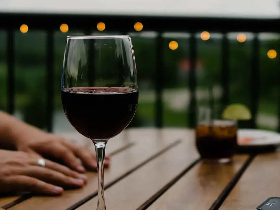 Verre de vin rouge posé sur une table en bois de terrasse, guirlande lumineuse floue en arrière-plan